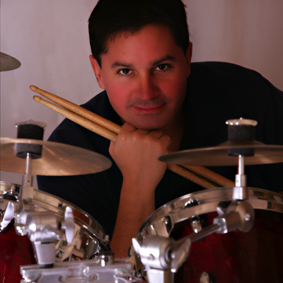 A man is sitting behind some drums and sticks