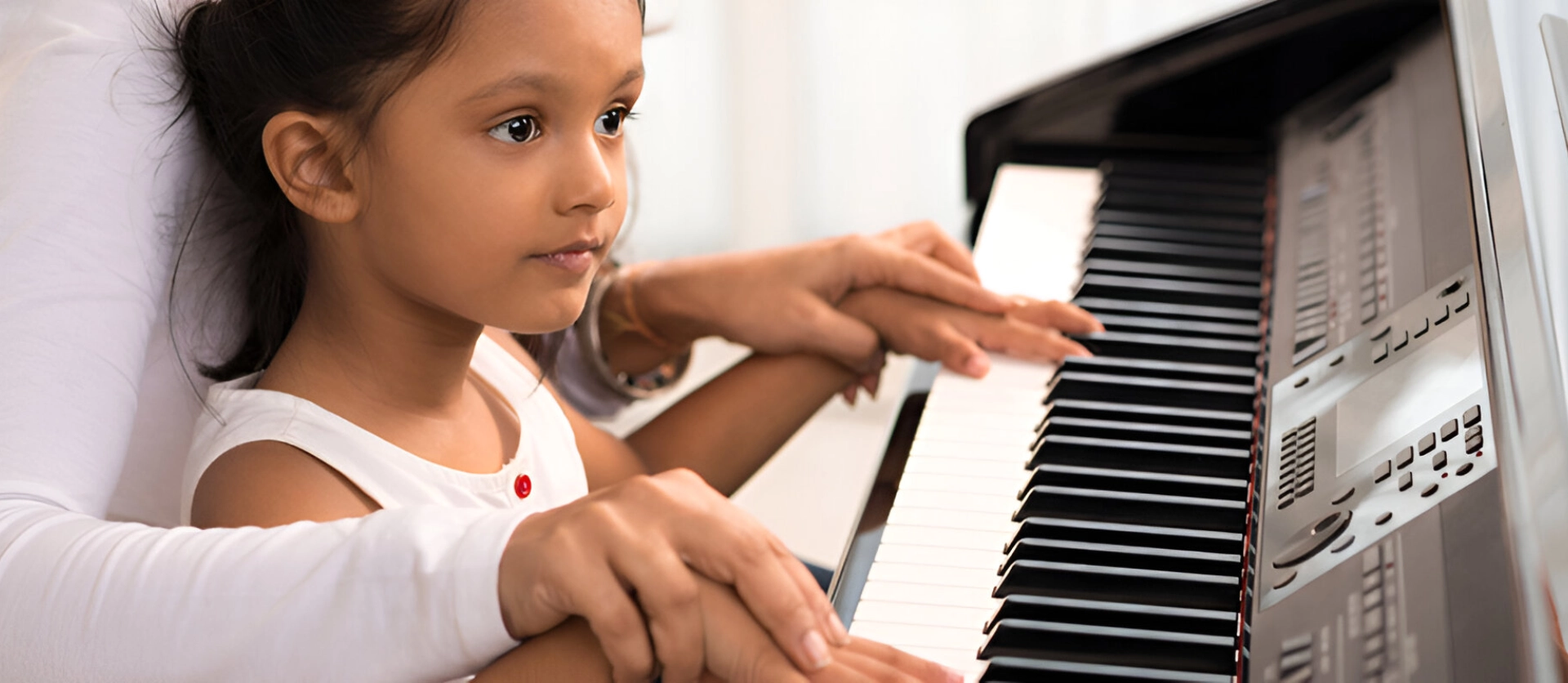 A little girl sitting at the piano with her hands on the keys.