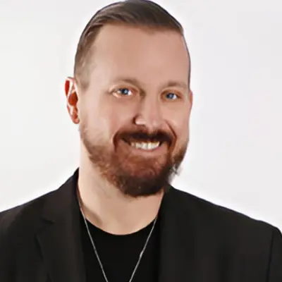 A man with beard and black jacket smiling.